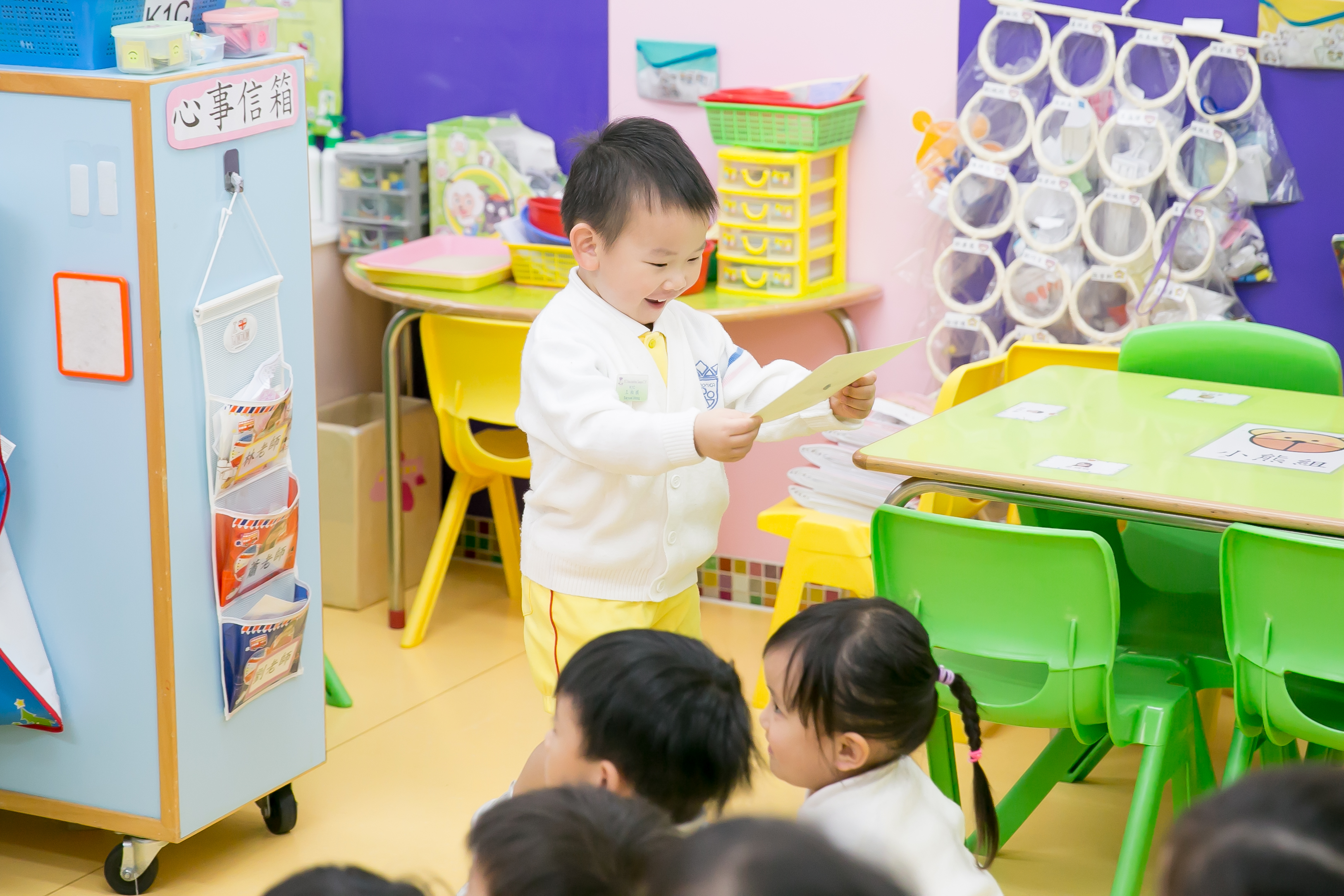 cute little boy is looking at something and smiling happily in the middle of a TEFL classroom