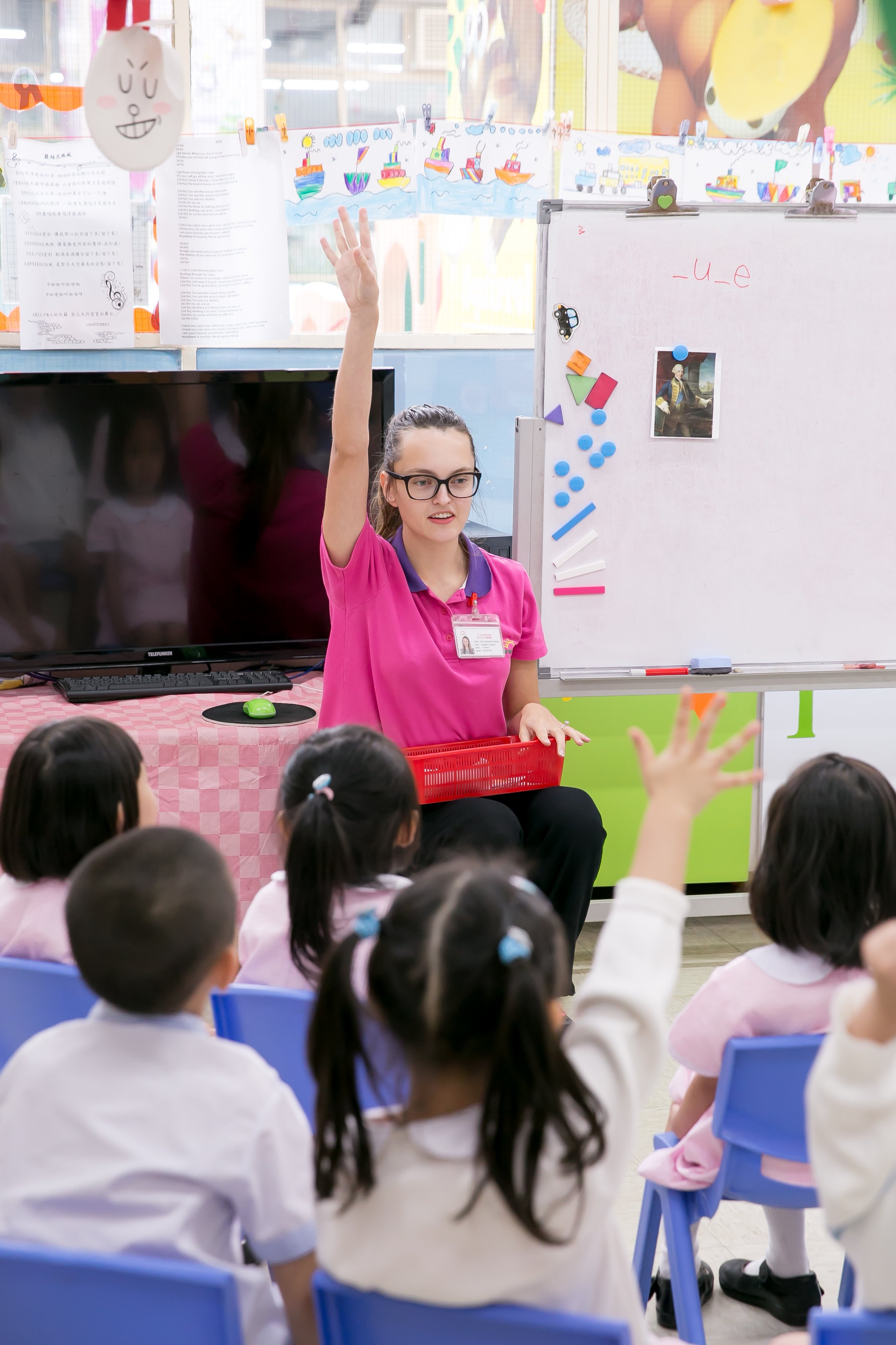 a TEFL teacher in pink t-shirt is encouraging children to participate in the lesson